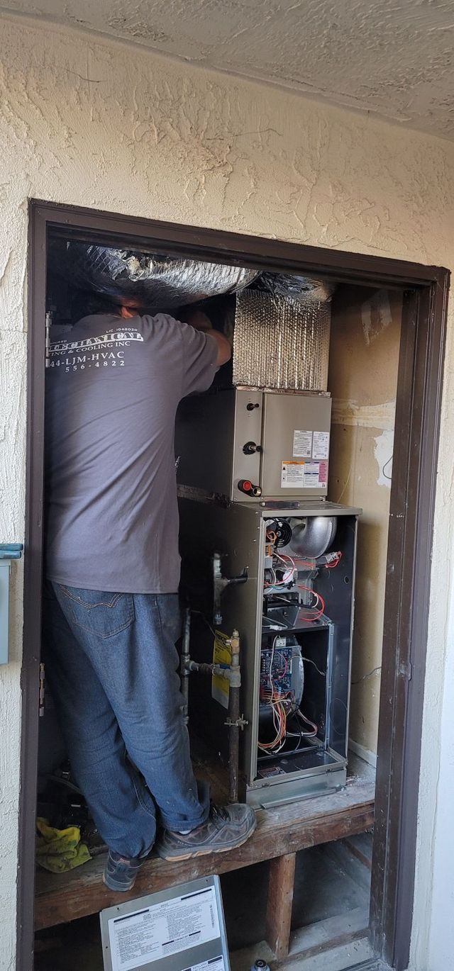 A person is working on a heating and air conditioning unit inside a wooden frame.