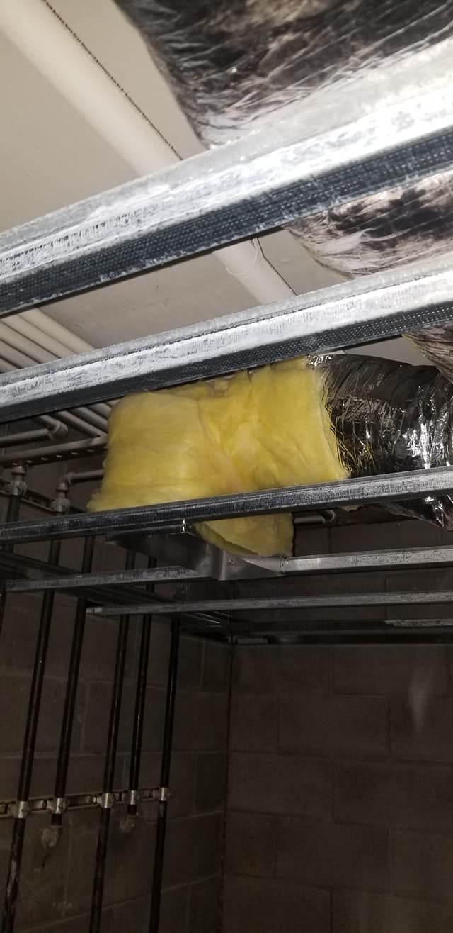 Yellow insulation wrapped in foil, installed within a metal frame in a dimly lit setting.