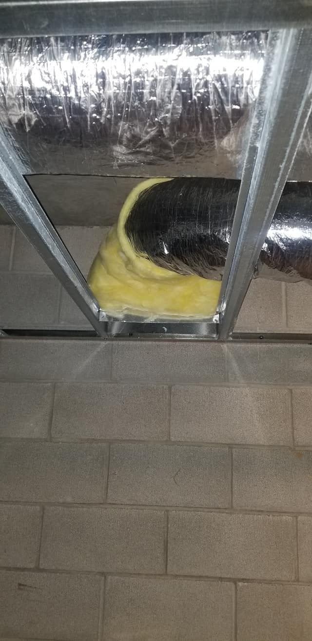 HVAC ductwork with insulation wrapping, installed in a metal frame. Brick wall below.