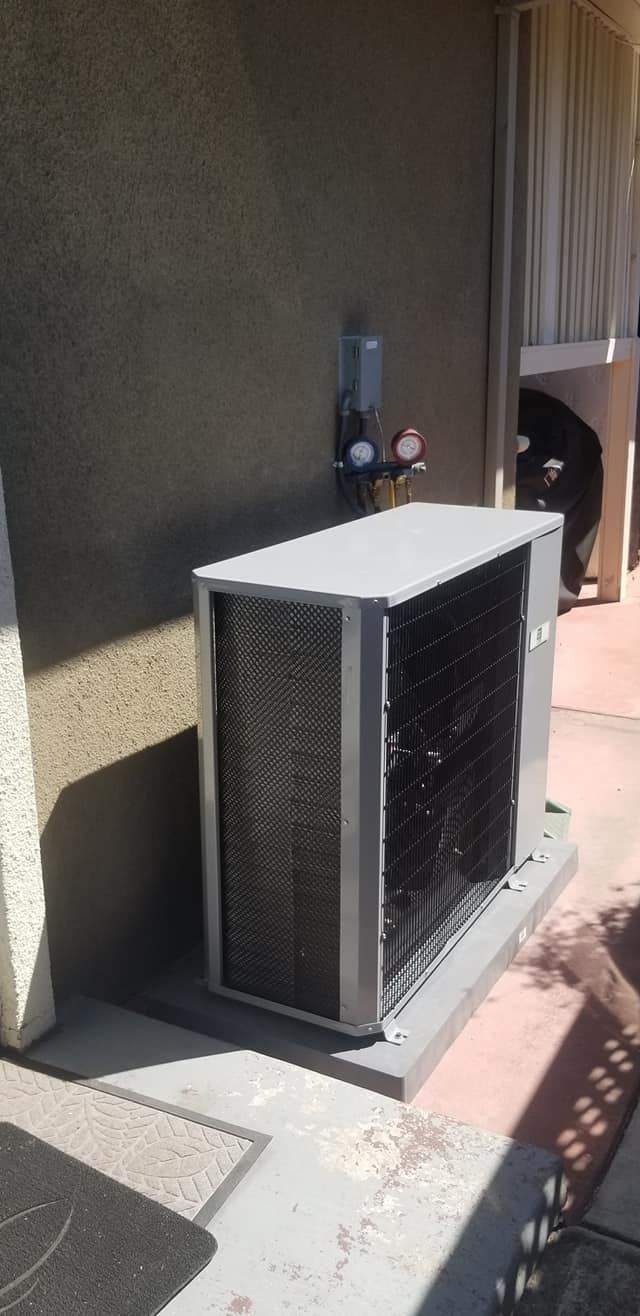 An air conditioning unit is against a stucco wall, with gauges on the wall, and sitting on a concrete pad.