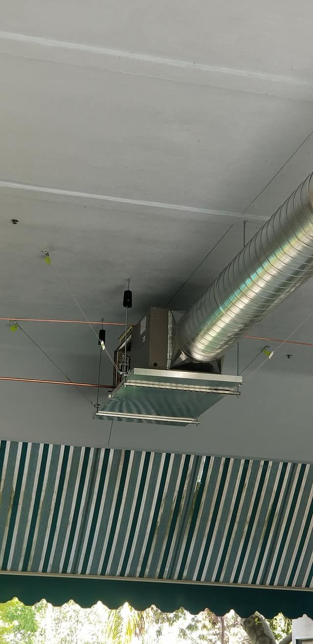 Ceiling fan with corrugated metal blades, attached to a ceiling with ventilation ducts and a green and white awning.