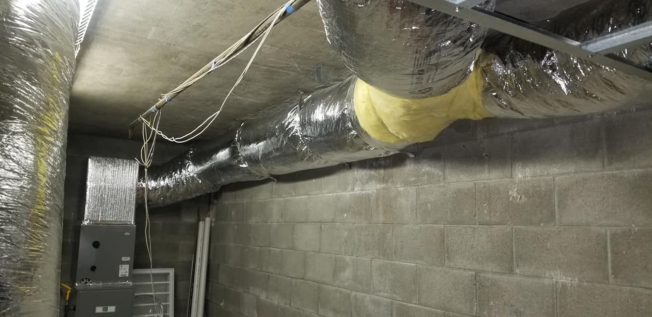 Ductwork and insulation in a concrete-block-walled basement. Electrical wires hang from the ceiling.