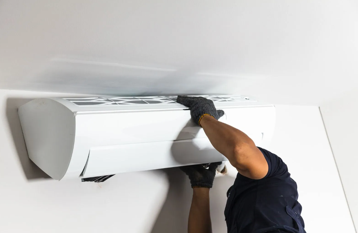 Person in blue gloves using a screwdriver to maintain a white air conditioning unit.
