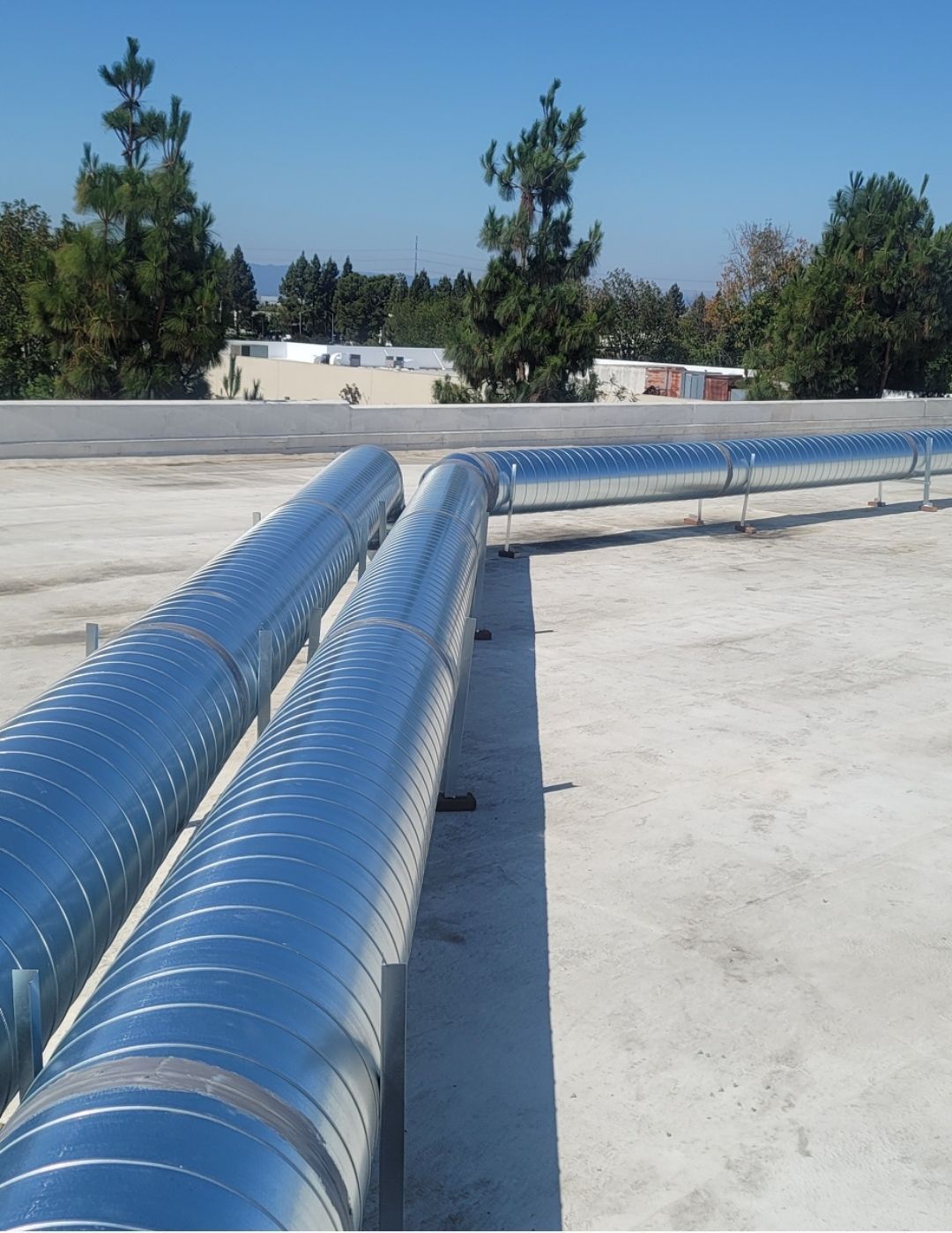 Silver insulated pipes running across a flat rooftop on a sunny day.