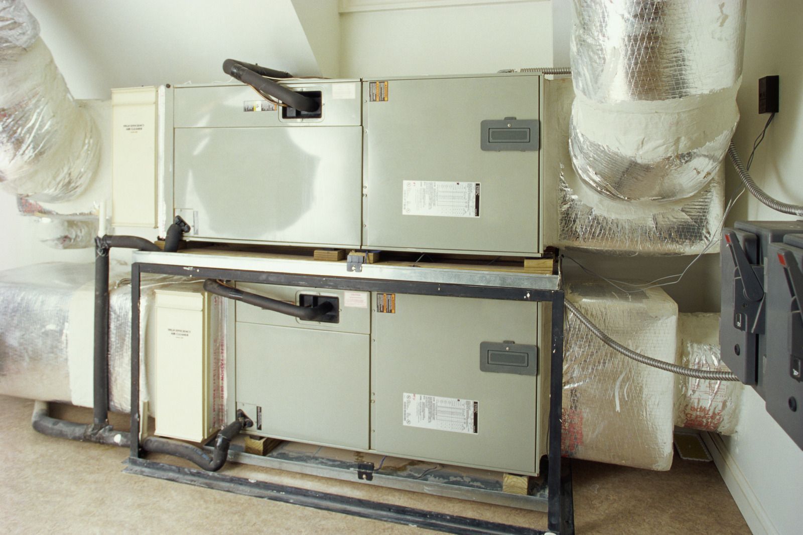 Stacked HVAC units with insulated ductwork. Grey metal units on a black metal frame in a room.