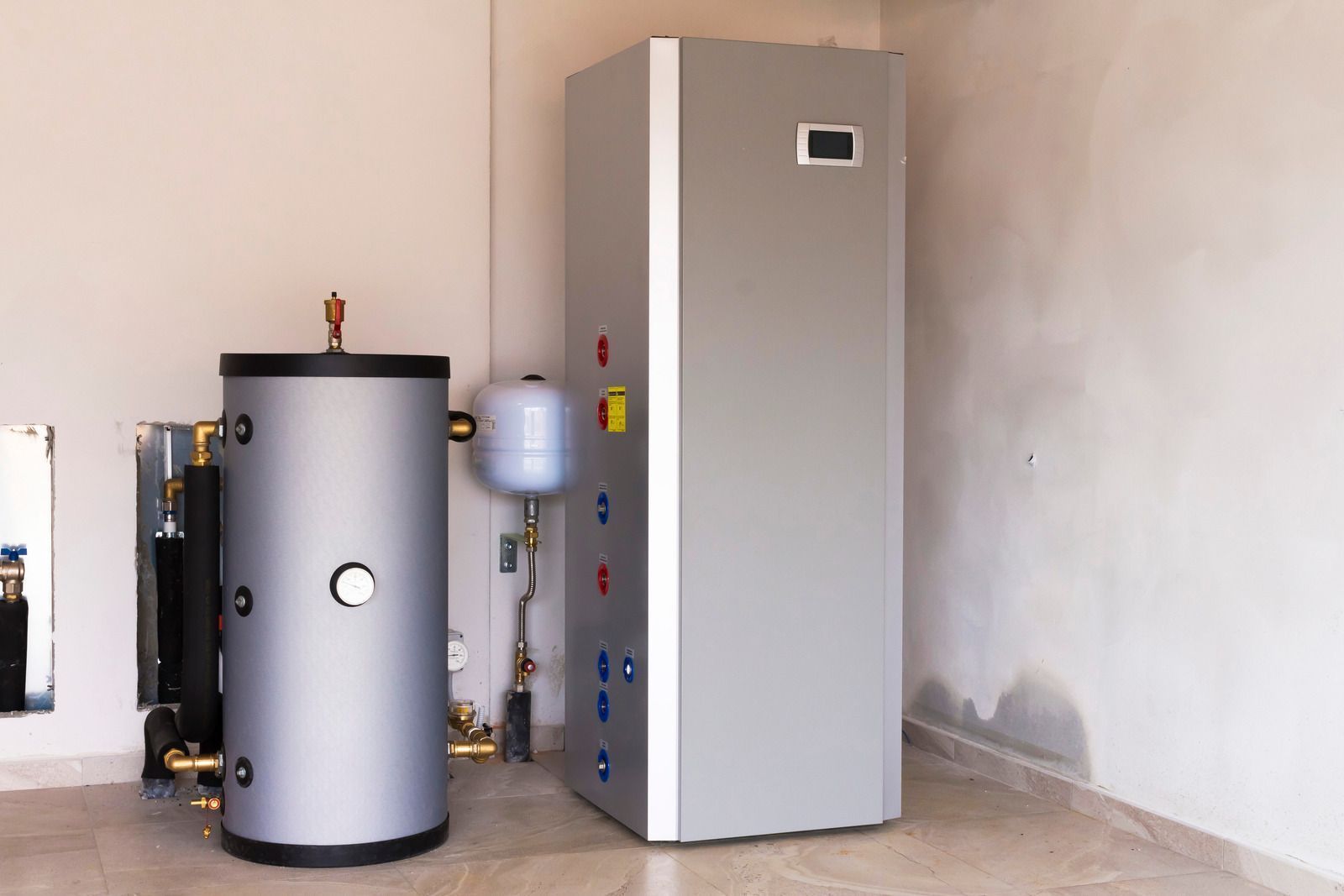Two silver heating units in a room with white walls, pipes and components visible.
