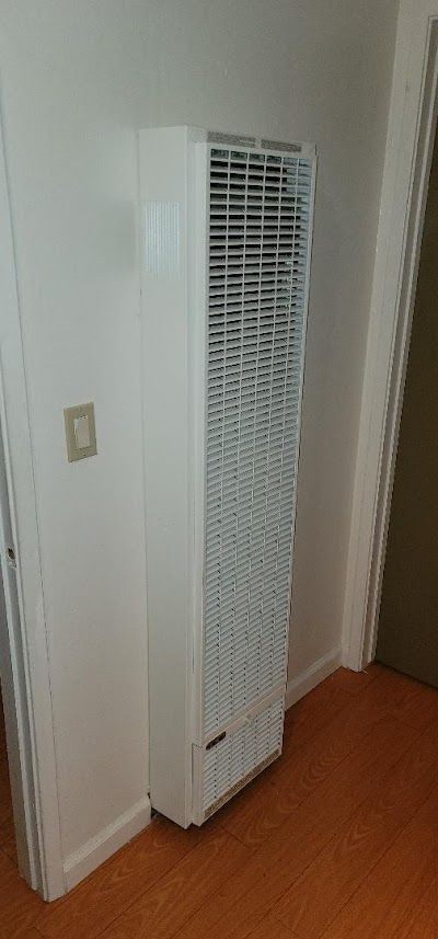 White wall-mounted heater in a room with wood-like floors and a light switch.