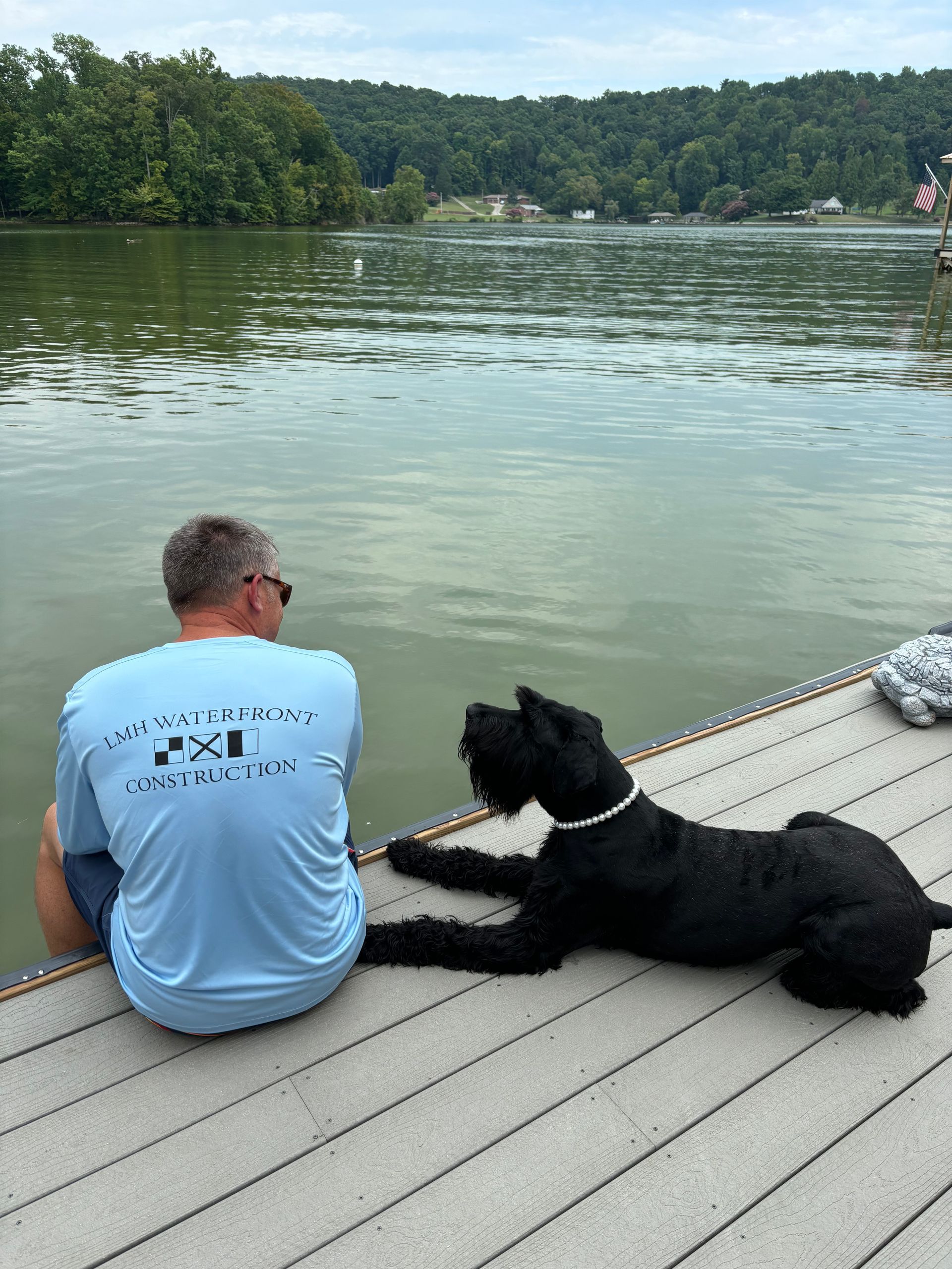 A man and a dog are sitting on a dock looking at the water.