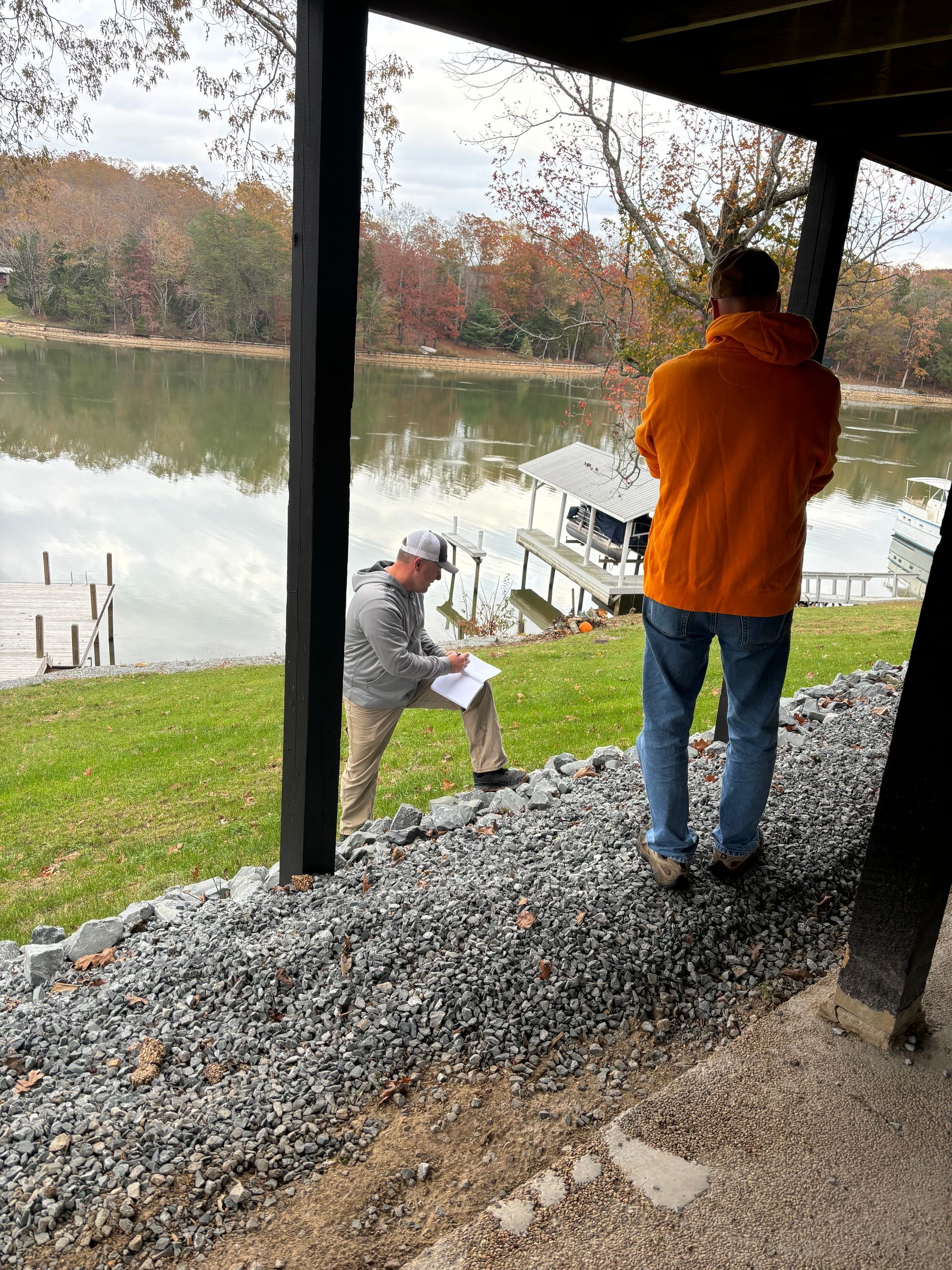 Two men are standing on a pile of gravel next to a lake.