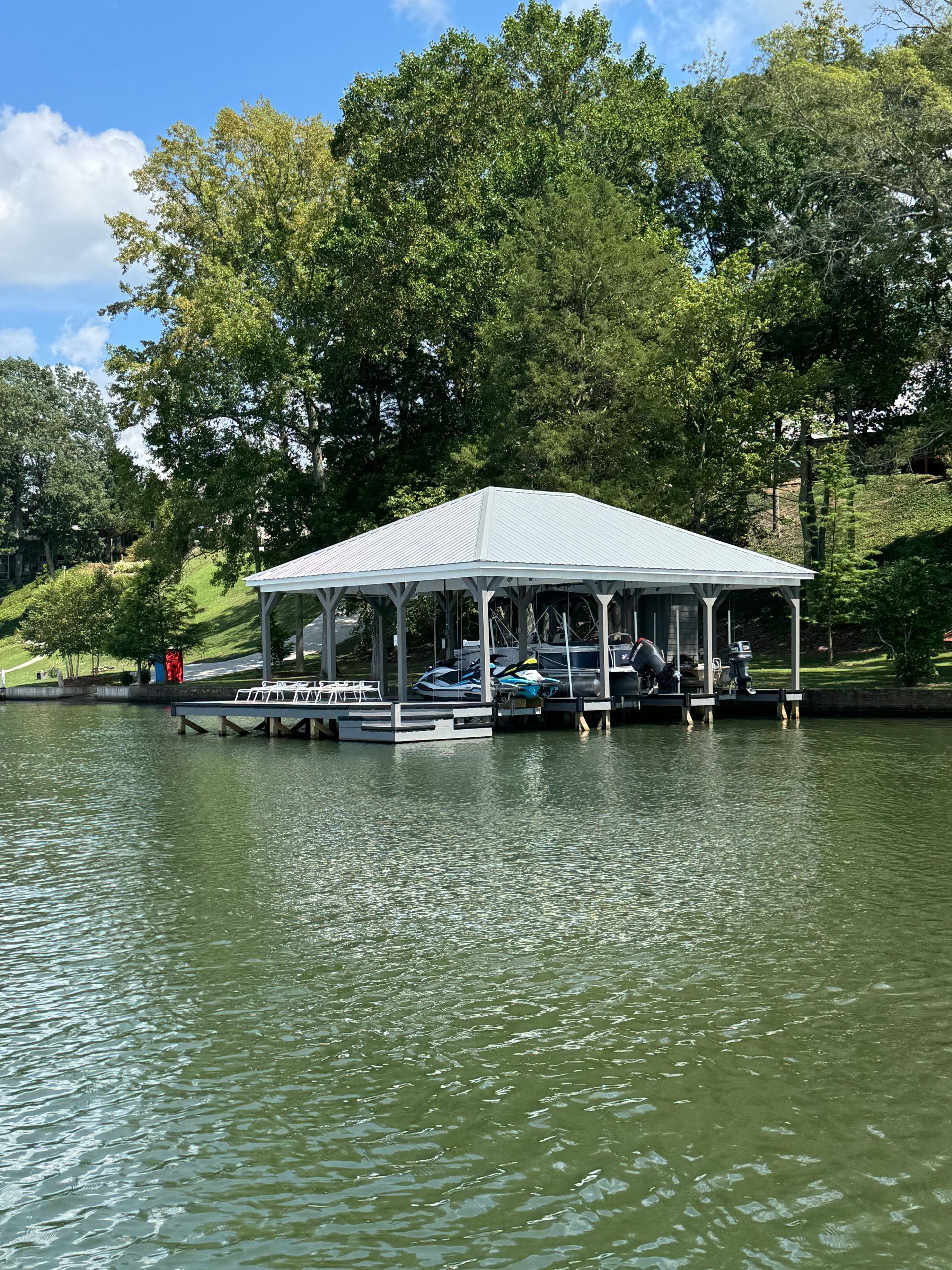 Boat dock on a lake, with boats under a white roof, surrounded by trees and a cloudy sky.