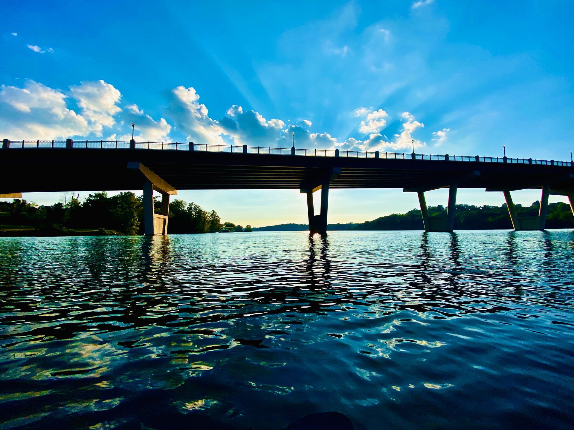 A bridge over a body of water with the sun shining through the clouds