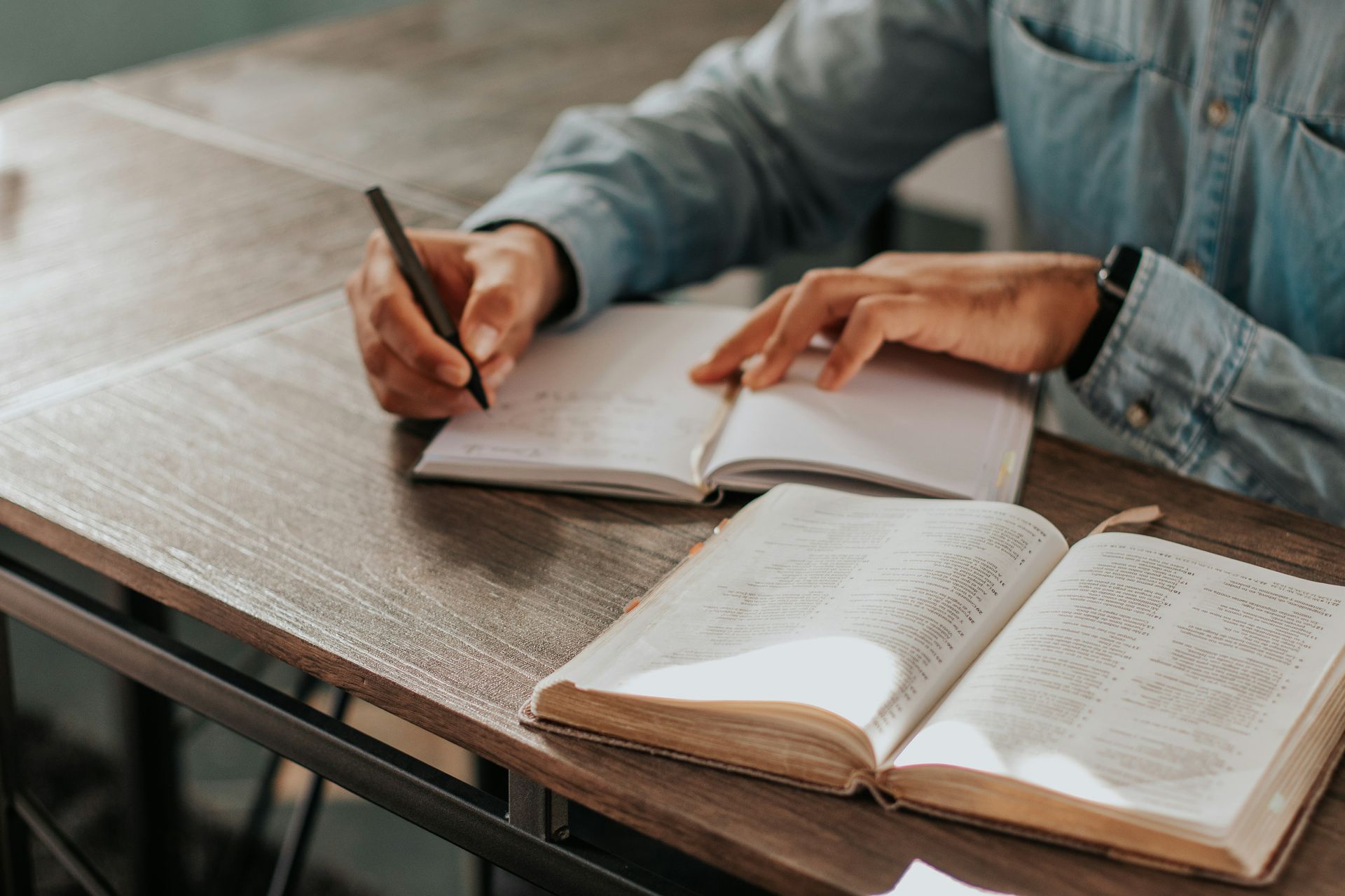 A person is sitting at a table writing in a notebook.