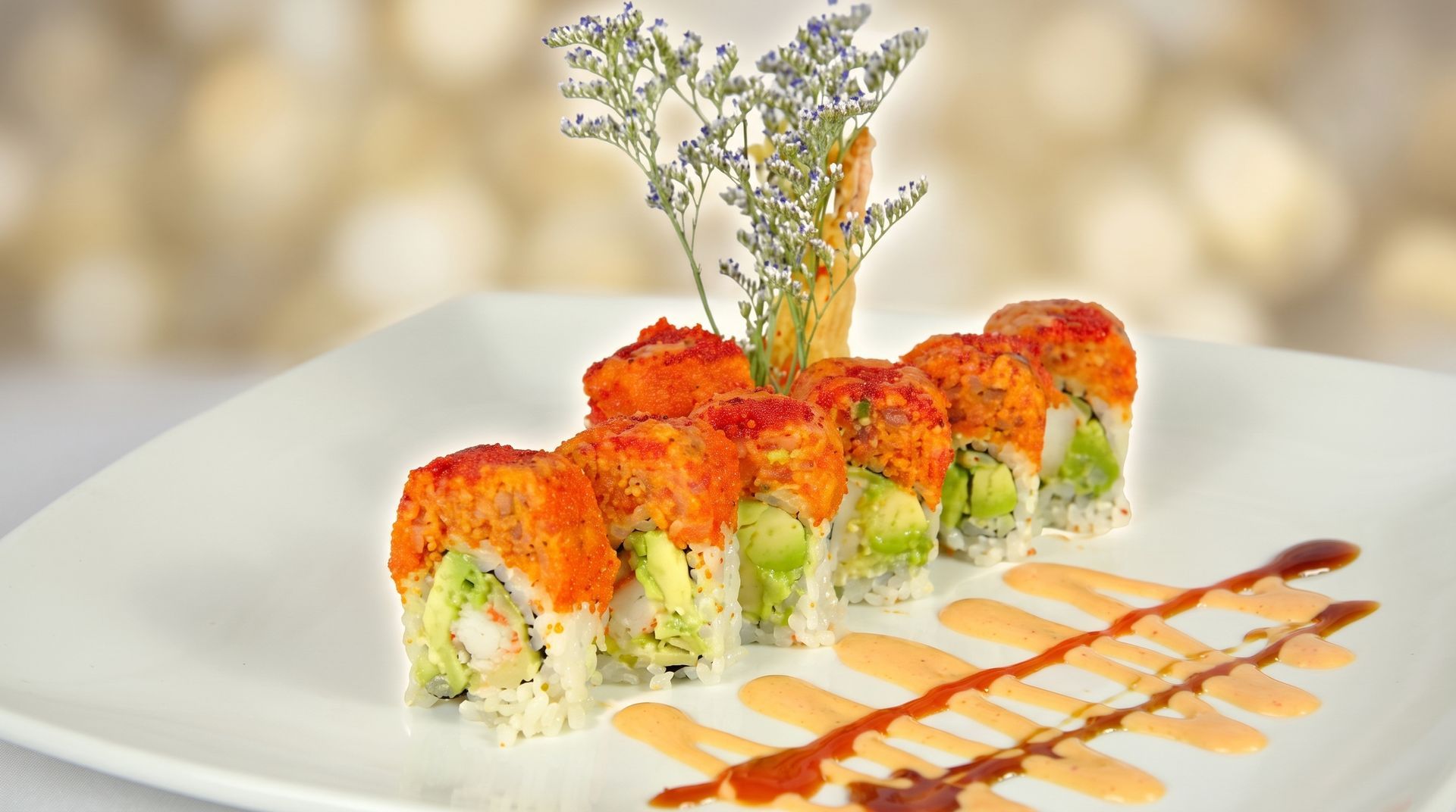 Sushi rolls topped with orange roe on a white plate, garnished with herbs and sauce drizzle