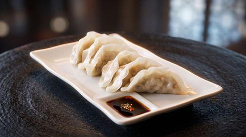 Steamed dumplings on a white plate with soy dipping sauce on a dark table