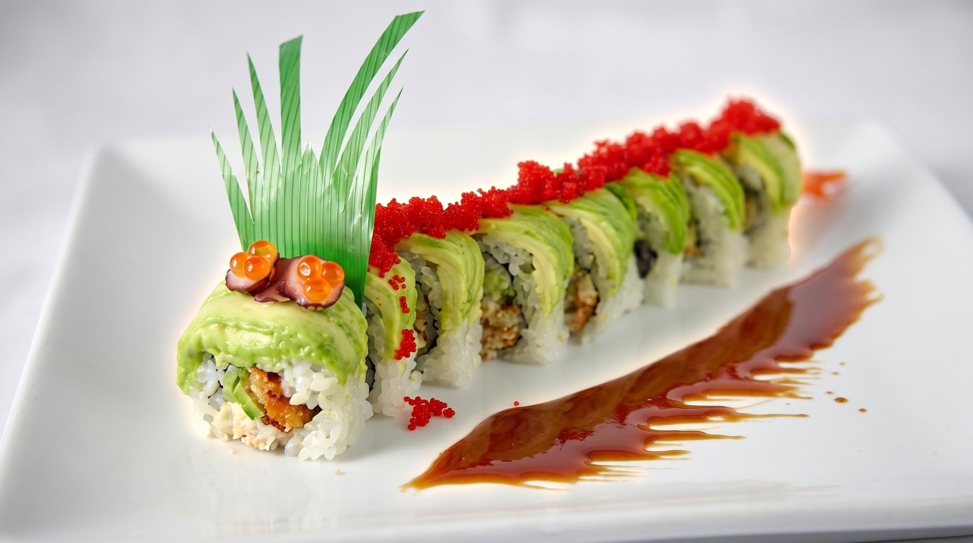 Sushi roll on a white plate, topped with red roe and green garnish, with sauce drizzled beside it