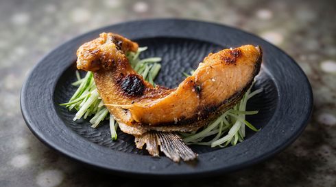 Grilled fish fillet on a black plate, garnished with shredded cucumber and herbs