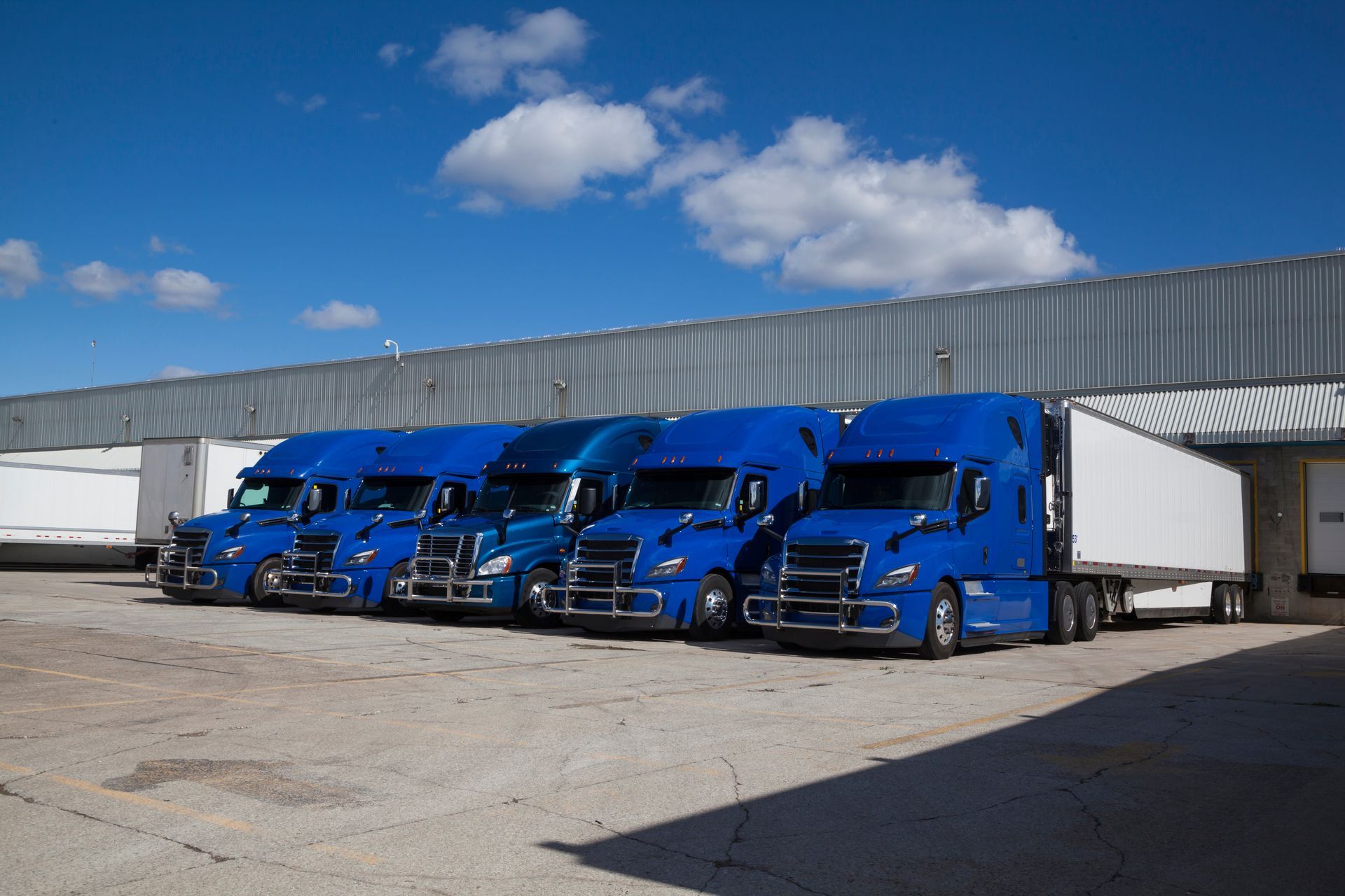 A row of blue semi trucks are parked in front of a building.