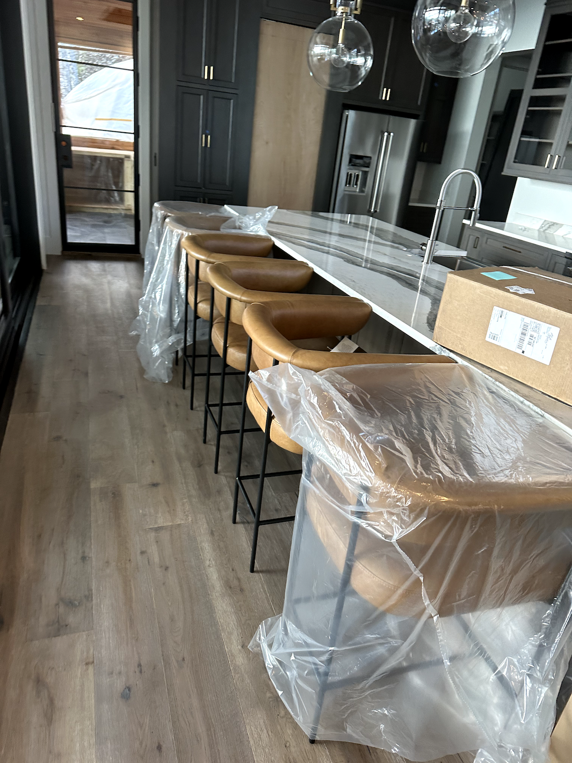 A kitchen with a bar and stools wrapped in plastic.