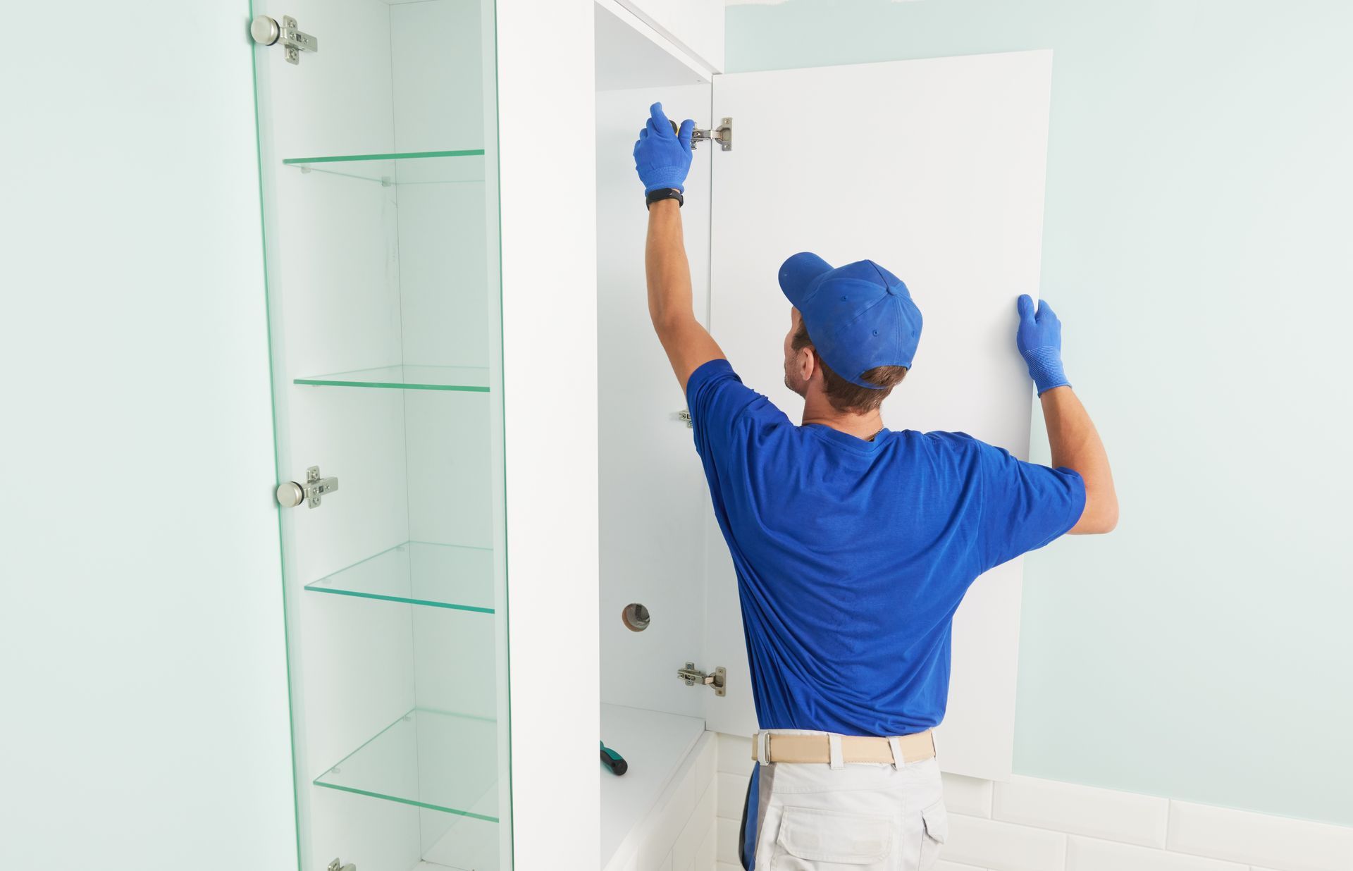 A man in a blue shirt and blue gloves is working on a cabinet.
