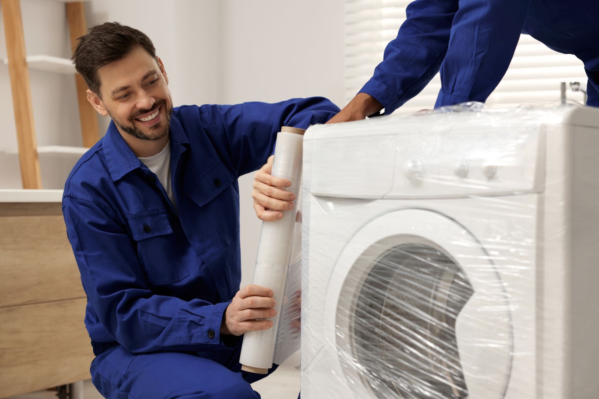 Two men are wrapping a washing machine with plastic wrap.