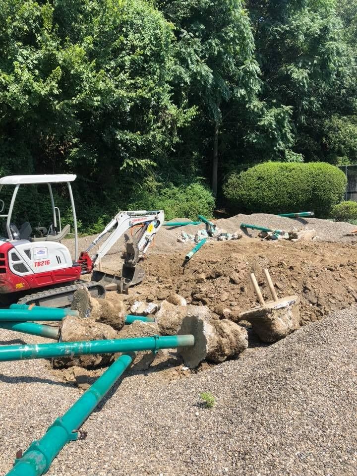 A construction site with a red-and-white excavator parked next to excavated dirt, green poles, and concrete footings.