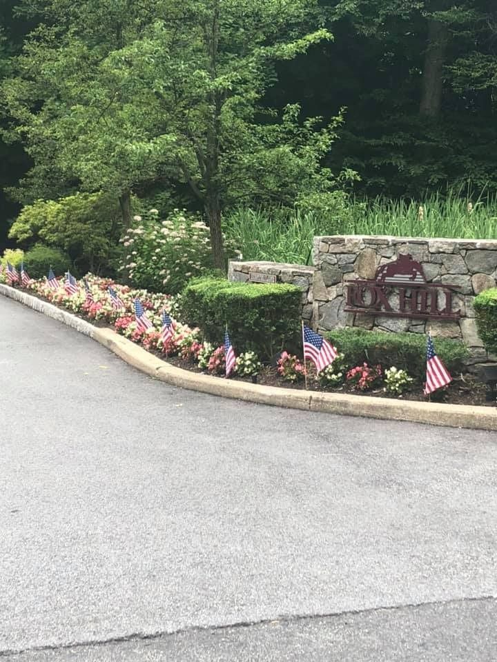 A stone entrance sign for Oak Hill, surrounded by landscaping decorated with a row of American flags.