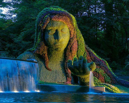 A statue of a woman is surrounded by trees and a waterfall