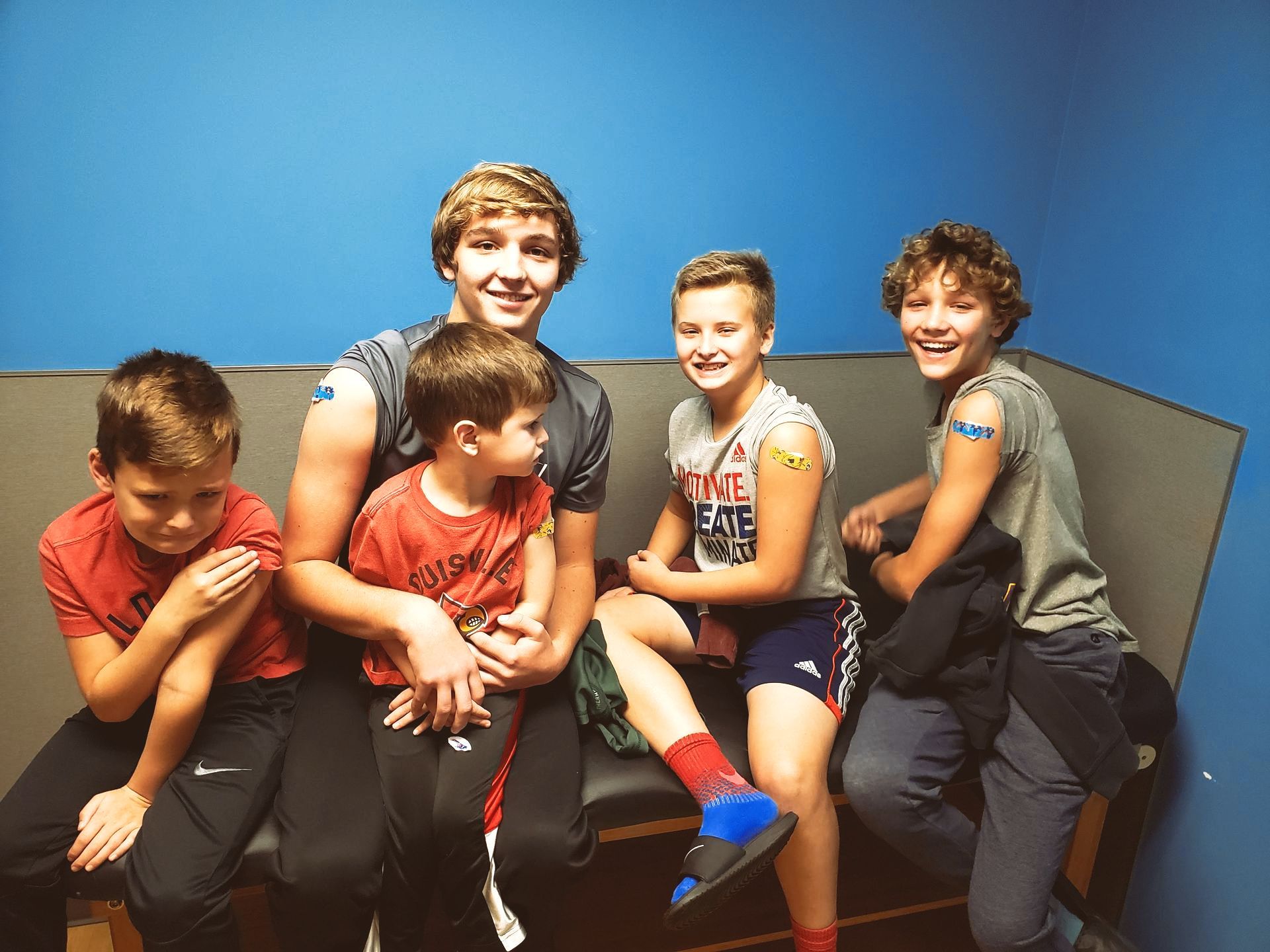 A group of young boys are sitting on a bench and one of them has a bandage on his arm