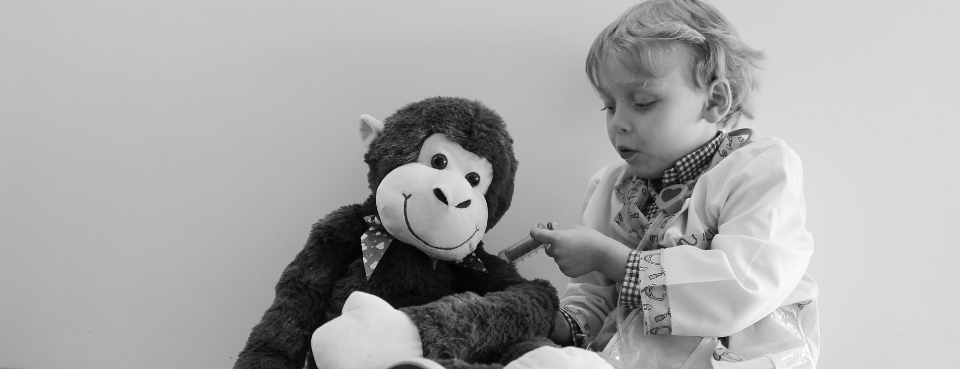 A young child pretending to give a stuffed monkey a shot.