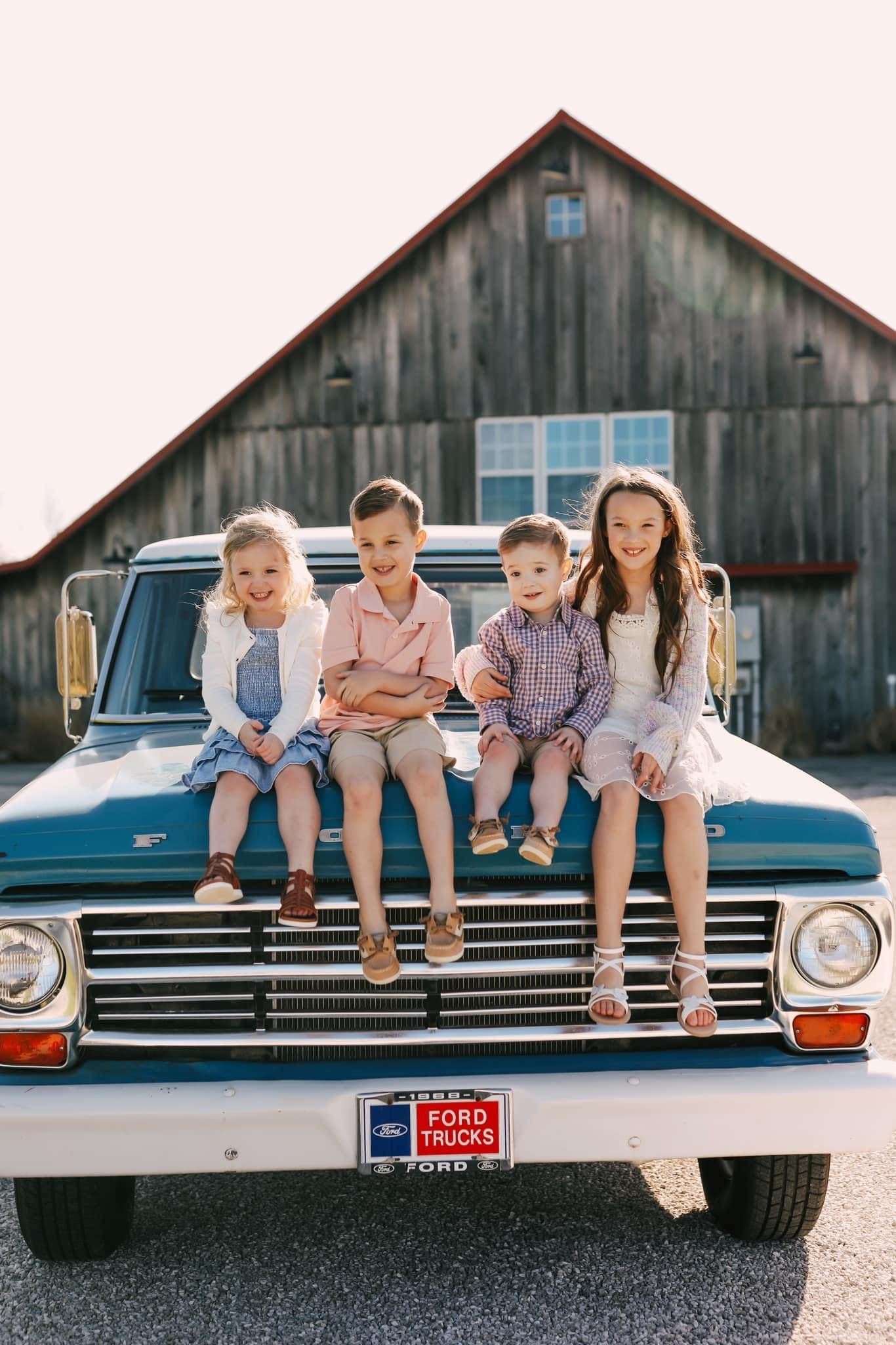 A group of children are sitting on the hood of a truck.