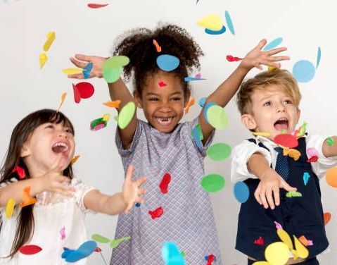 Three young children throwing confetti in the air and smiling.