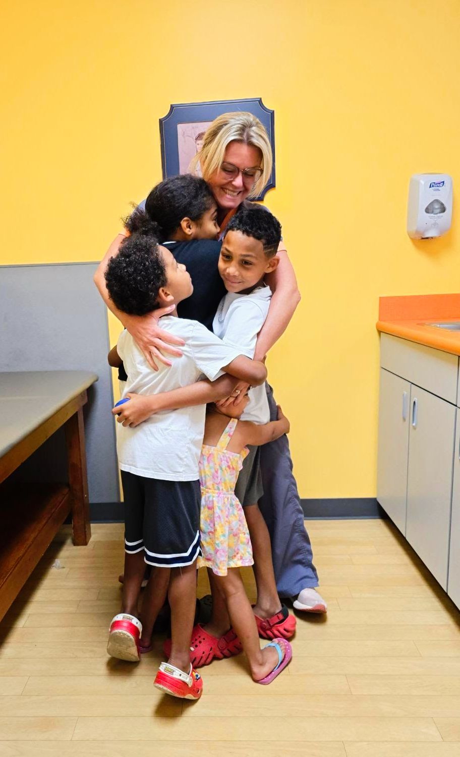 Female medical professional hugging three children in an exam room.