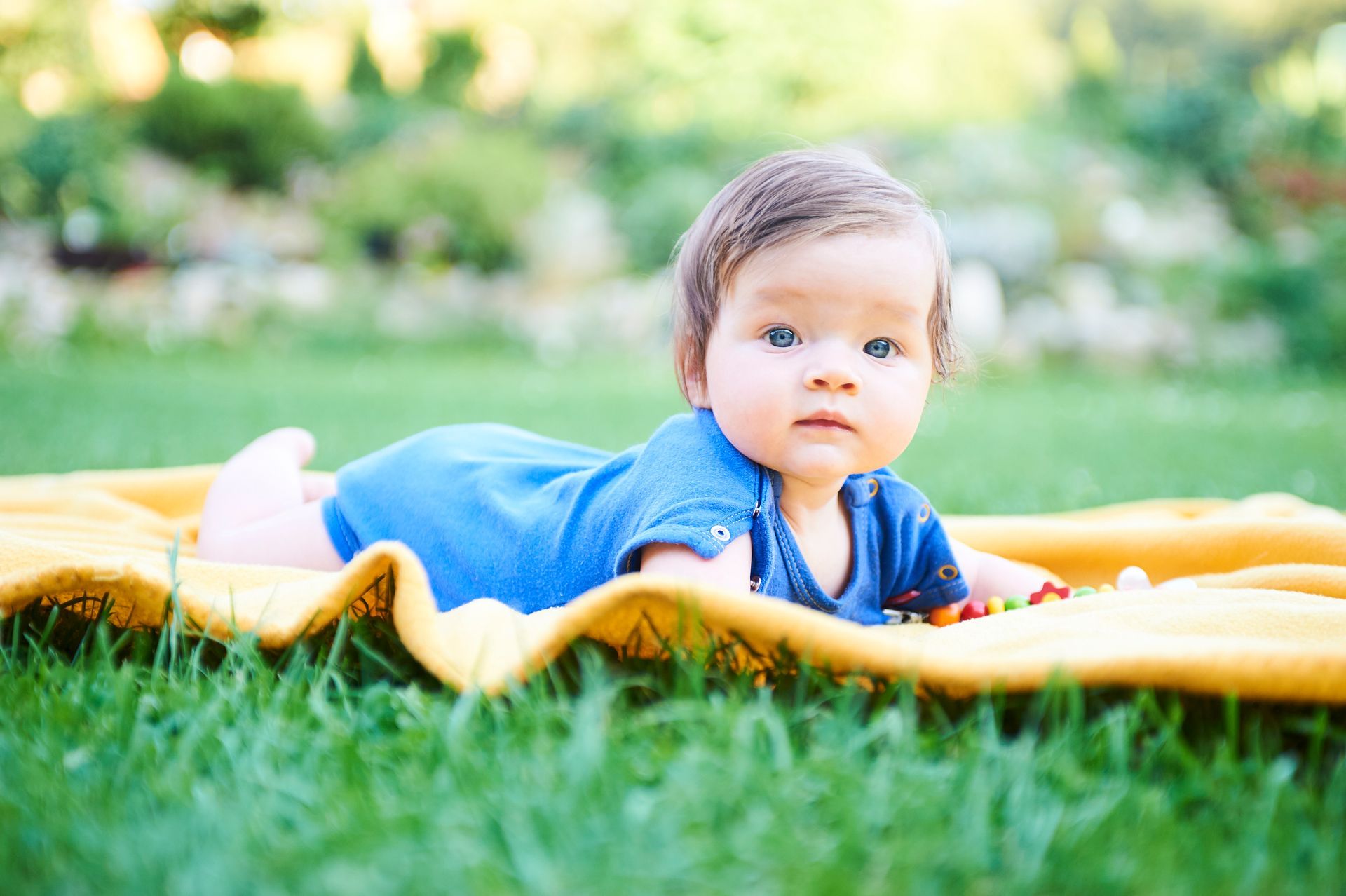 Baby laying on blanket in a park.