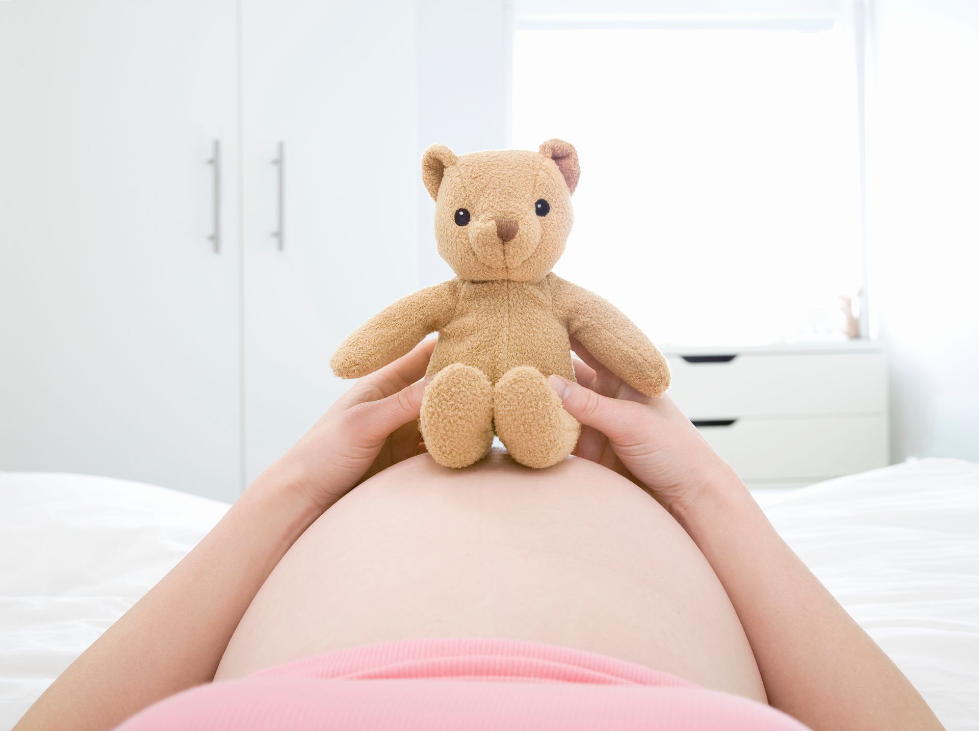 Teddy bear sitting on top of a pregnant woman's belly.
