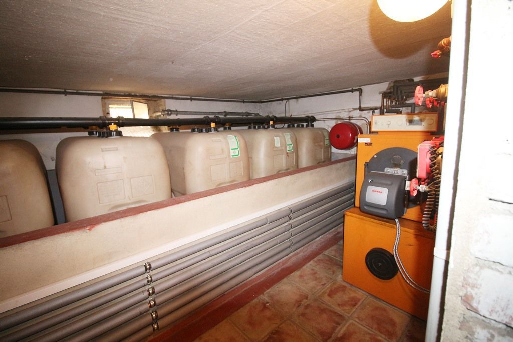 Großer Industrieraum mit Reihen beiger Tanks, Rohrleitungen und einer orangefarbenen Maschine an der Wand.