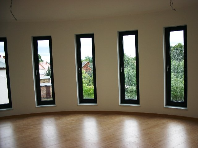 Leerer Raum mit gebogener Wand, fünf hohen, schmalen Fenstern und hellem Holzboden.
