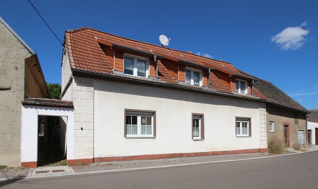 Weißes Haus mit rotem Ziegeldach neben einer Straße unter blauem Himmel