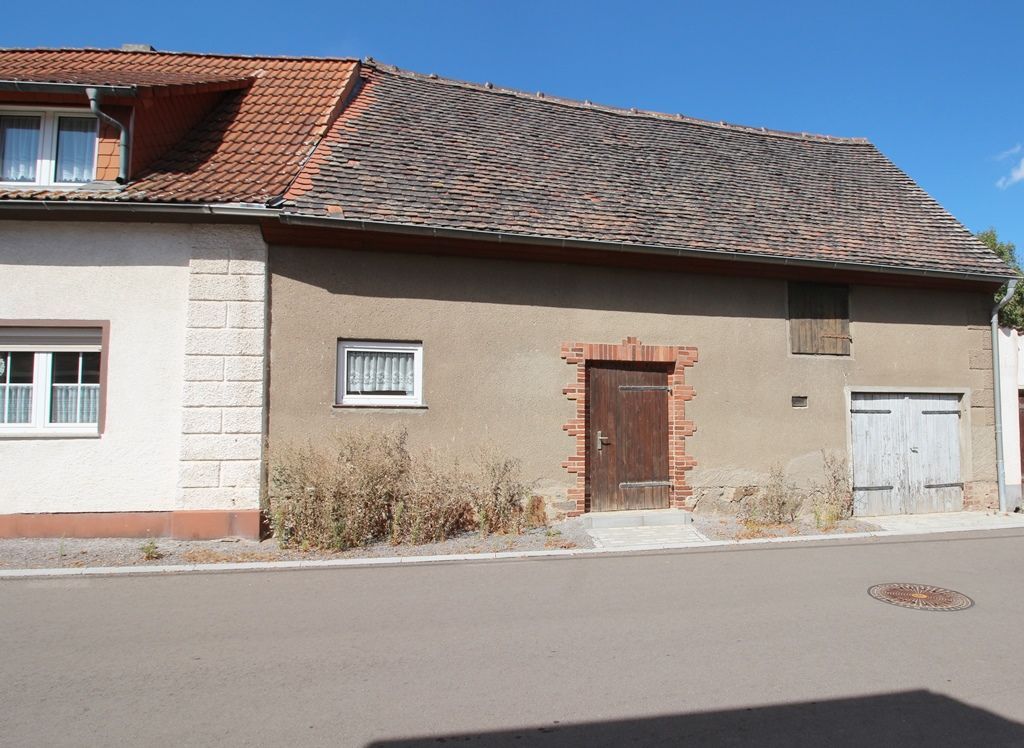 Altes beiges Haus mit rotem Ziegeldach und kleinen Fenstern an einer gepflasterten Straße