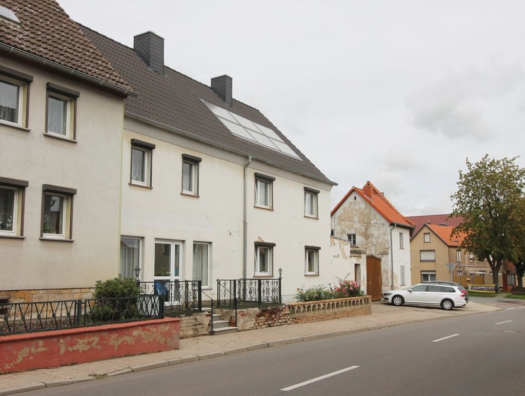 Wohnstraße mit weißen Häusern, geparkten Autos und bedecktem Himmel