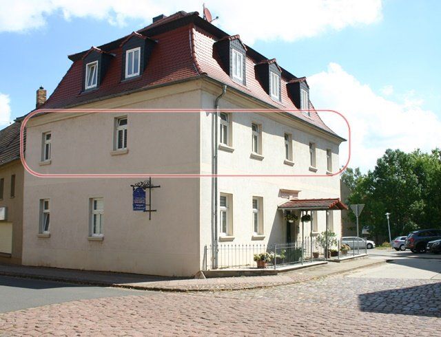 Dreistöckiges beigefarbenes Haus mit rotem Dach in einer Kopfsteinpflasterstraße, rosa umrandet.