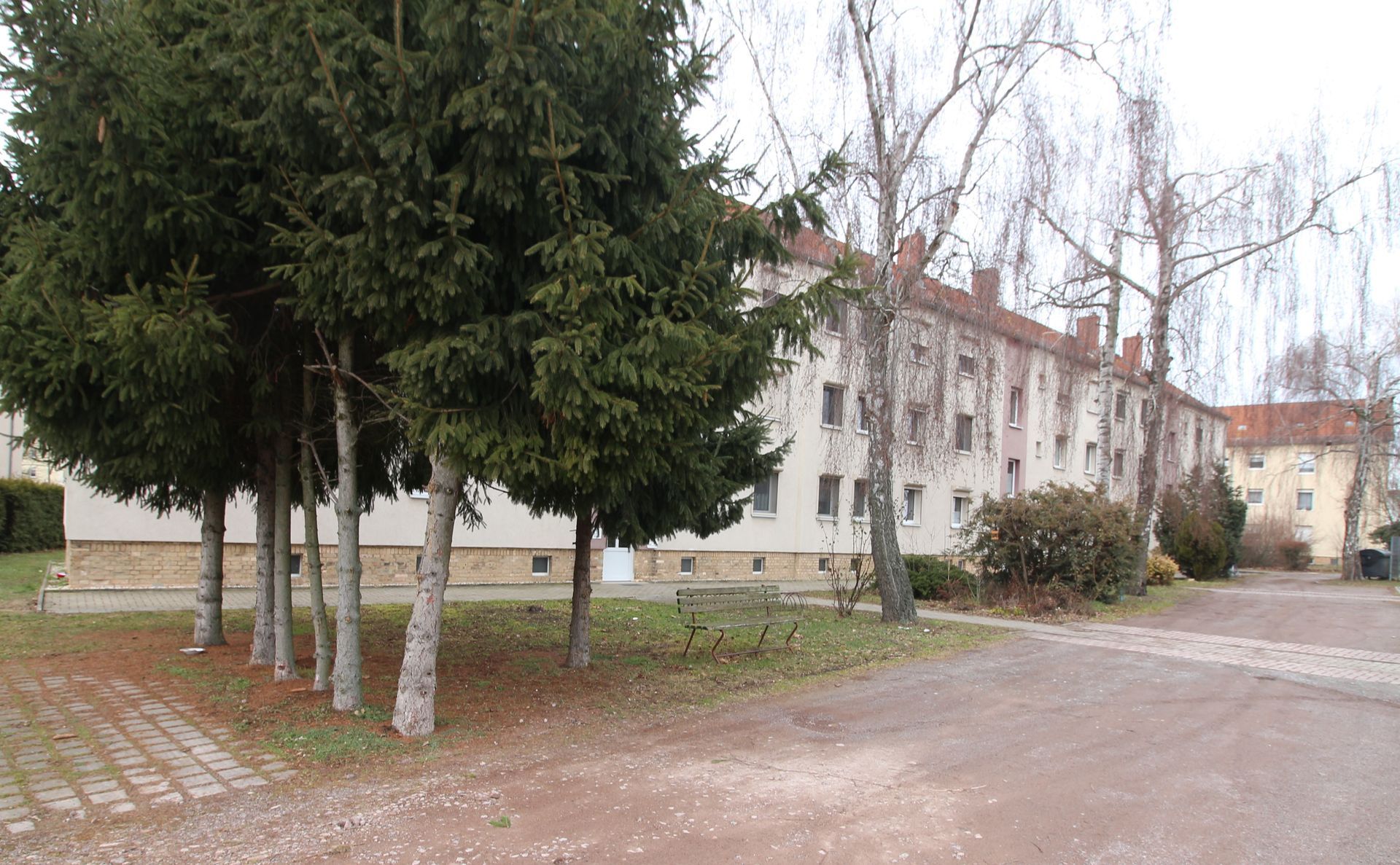 Ein von Bäumen gesäumter Innenhof neben einem weißen Wohnhaus an einem bewölkten Tag