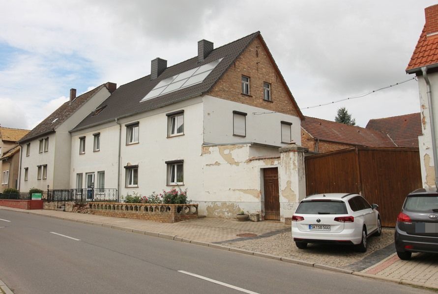 Straßenansicht eines weißen Hauses mit braunem Dach und geparkten Autos an einer ruhigen Straße