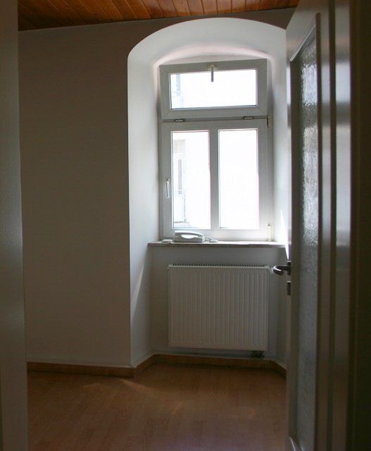 Leerer Flur mit Fenster, Heizkörper, weißen Wänden und Holzboden.