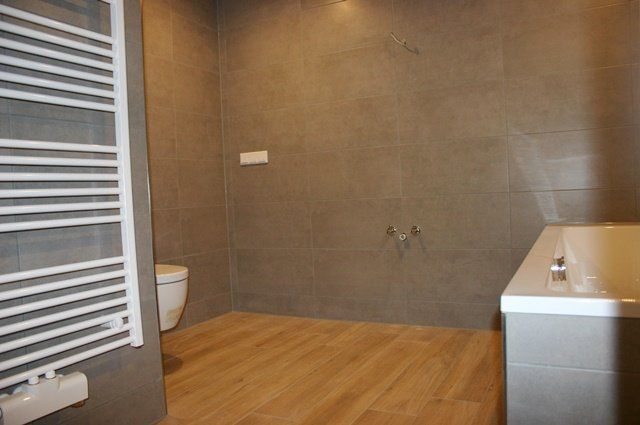 Modernes Badezimmer mit Holzboden, grauen Fliesenwänden, WC, Handtuchheizkörper und weißem Waschtisch