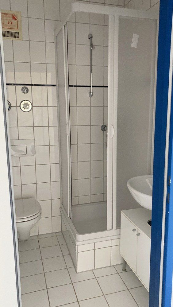 Barrierefreie Duschkabine in einem gefliesten Badezimmer mit Haltegriffen und einem Waschbecken in der Nähe