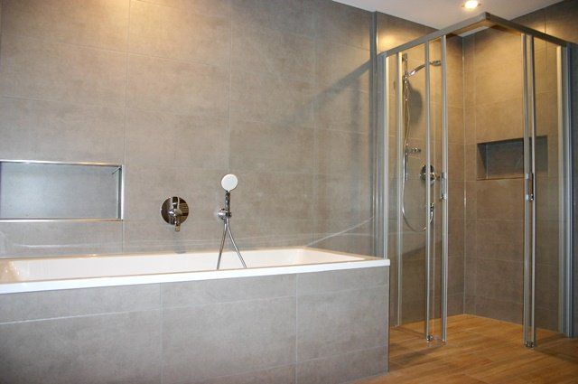 Modernes Badezimmer mit großer Badewanne, gefliesten Wänden und verglaster Dusche in warmem Licht
