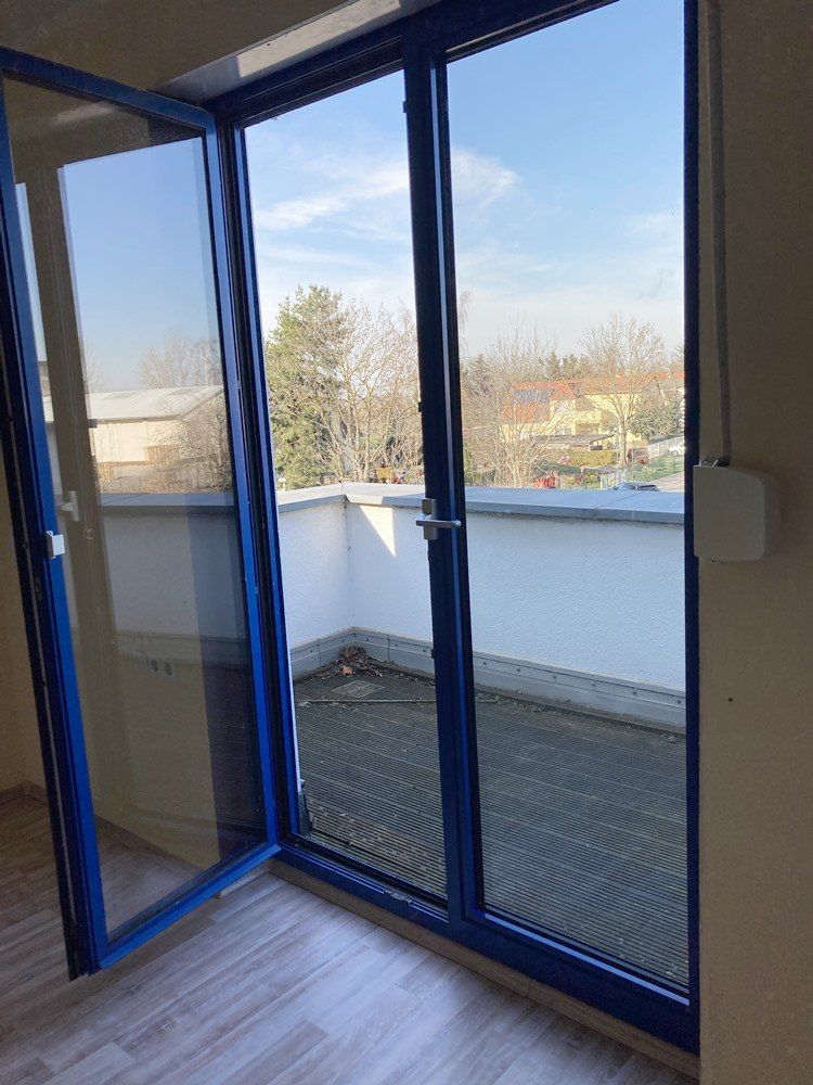 Öffnen Sie die blau umrandeten Glastüren zum Balkon, die auf eine kleine Terrasse mit Stadtblick führen.
