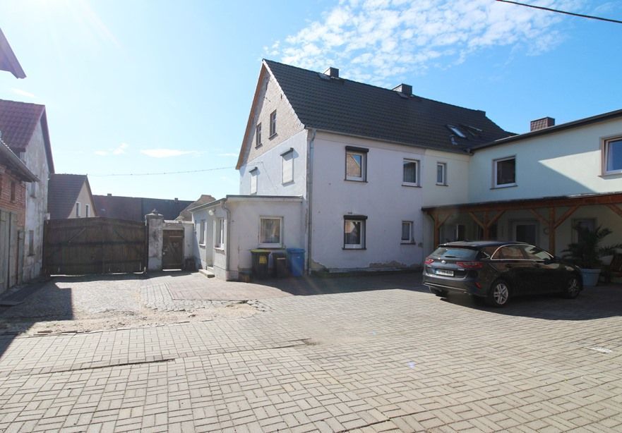 Gepflasterter Innenhof mit einem weißen Haus, geparkten Autos und blauem Himmel