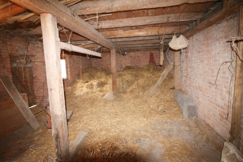 Leeres, mit Heu gefülltes Scheuneninneres mit Holzbalken und groben Ziegelwänden