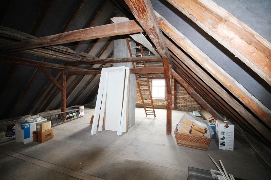Unfertiger Dachboden mit freiliegenden Holzbalken, Dämmmaterial und auf dem Boden verstreuten Baumaterialien.